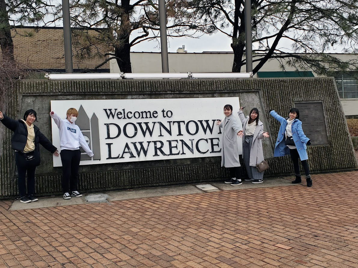 Students posing in front of the "Welcome to Downtown Lawrence" sign